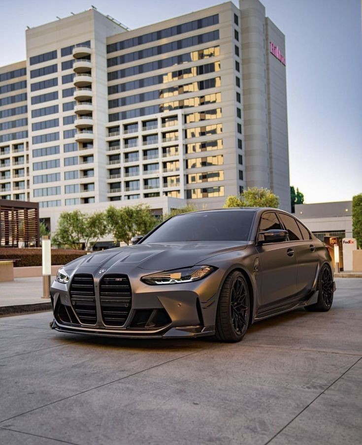 Sleek black car parked in front of a tall modern building under clear skies.
