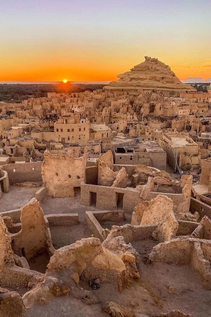 Sunset over ancient desert village with rocky structures and ruins.