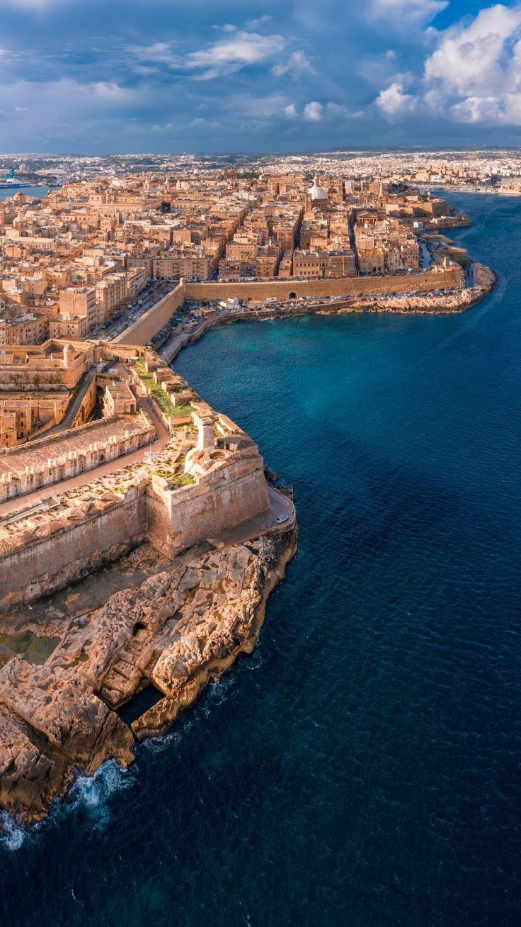 Aerial view of a historical fortified city by the sea with ancient buildings and rocky coastline.
